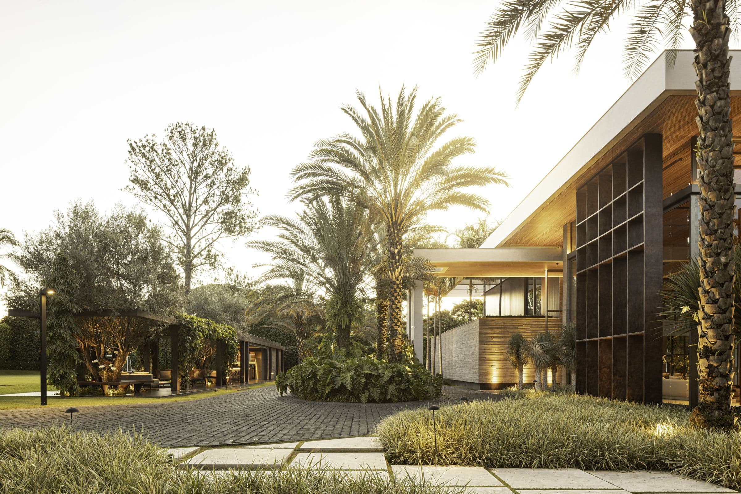 Casa da TECNA Home ao entardecer, entre palmeiras, com fachada de madeira e vidro