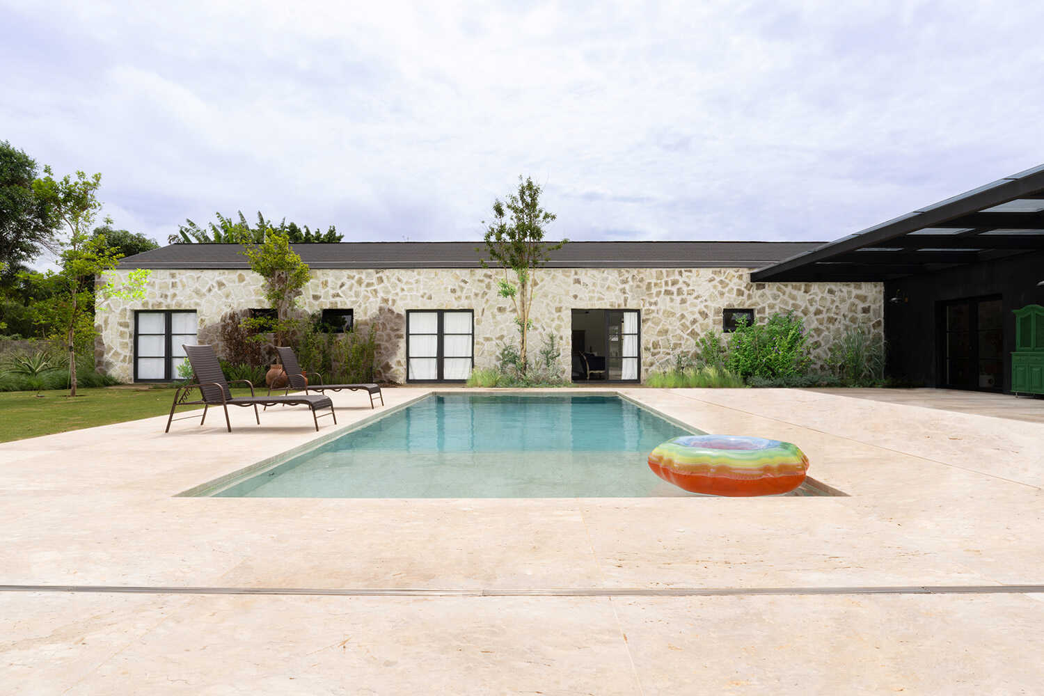 Piscina com deck de travertino e fachada de pedra