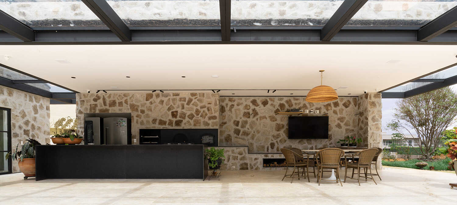 Cozinha externa coberta com parede de pedra e mesa de jantar